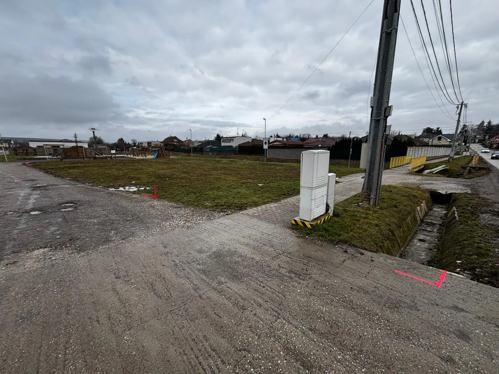 PRED — pôvodný stav pozemku v centre obce (~1 200 m²). Červené geodetické značky vyznačujú hranice budúcej stavby.