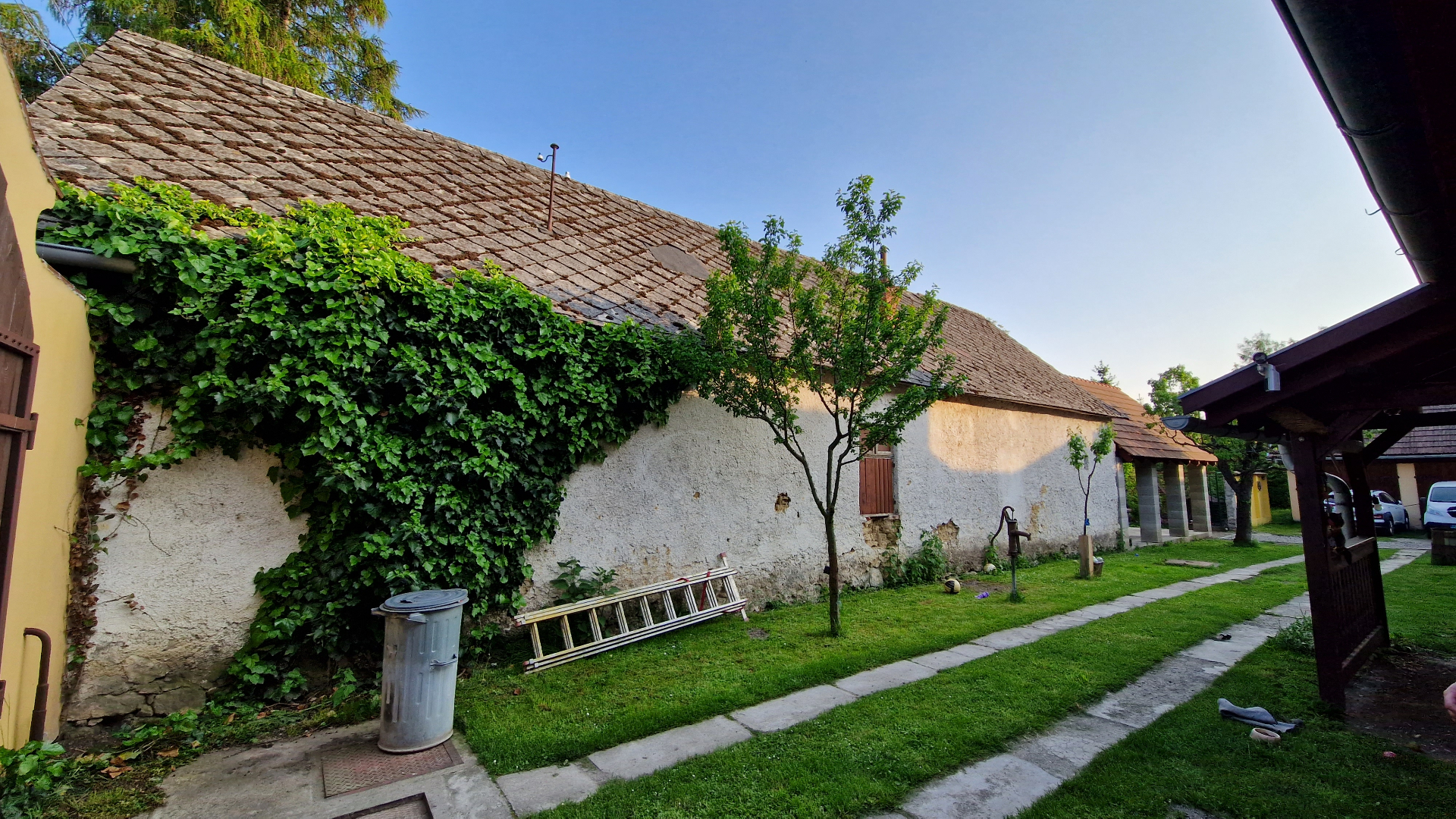 PRED rekonštrukciou (05/2023) — vnútorný dvor s hospodárskou budovou, pôvodnou pálenou krytinou, brečtanom porastenou stenou a starou ručnou pumpou