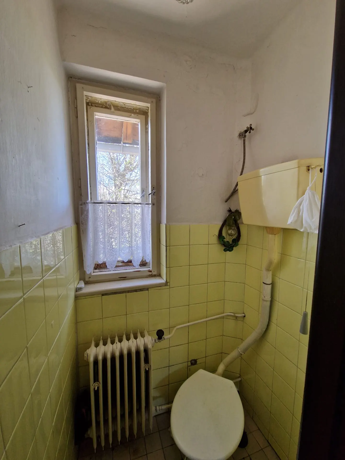 PRED rekonštrukciou (05/2025) — pôvodné WC so žltým obkladom, liatinovým radiátorom a starým splachovačom. Priestor bude kompletne vybúraný a nahradený novou dispozíciou.