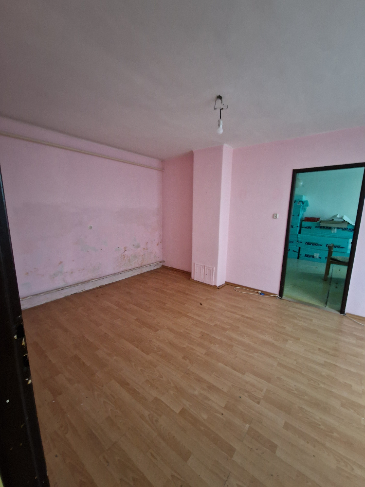 PRED rekonštrukciou (05/2025) — pôvodná izba s ružovými stenami, laminátovou podlahou a viditeľnými stopami vlhkosti pri sokli. Priestor čaká sanácia, nové povrchy a wellness-orientovaná dispozícia.